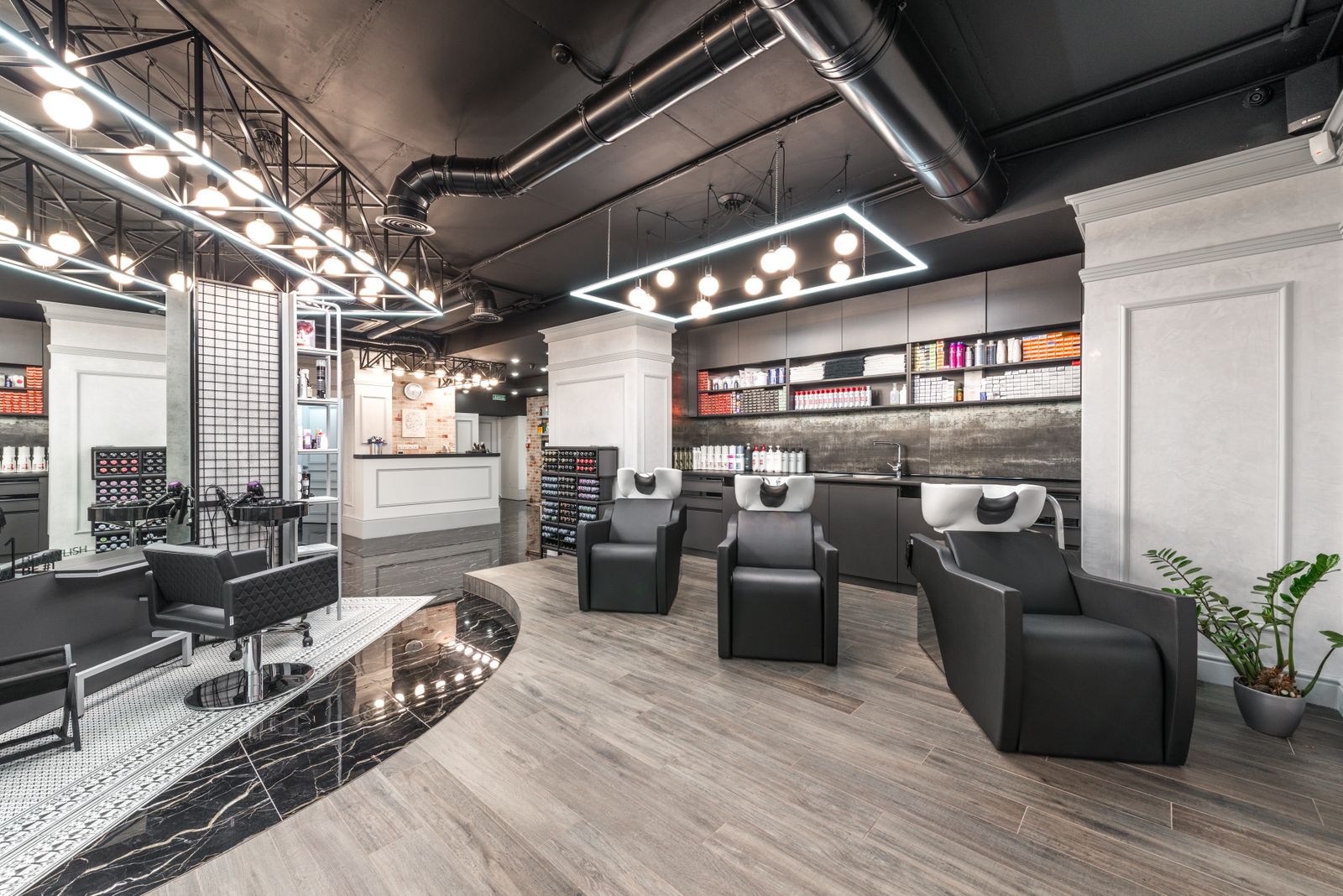 Comfortable backwash chairs with sinks near potted plant placed in contemporary beauty salon with bright illumination and abundance of cosmetology products